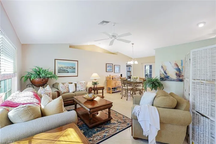 Tiled living room with ceiling fan with notable chandelier and lofted ceiling