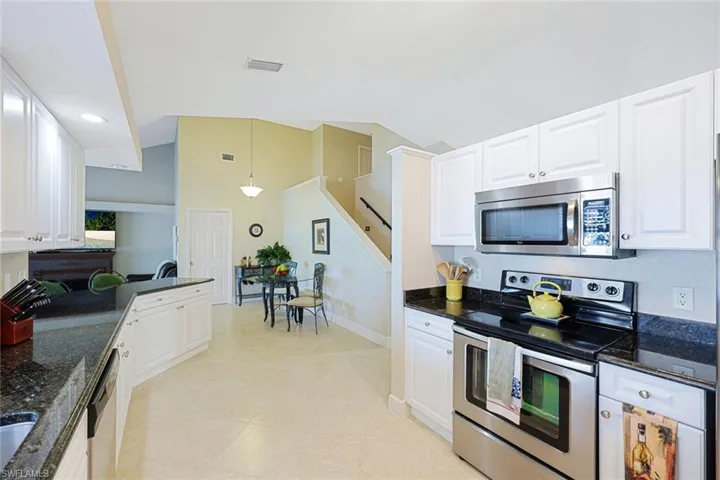 Kitchen featuring dark stone countertops, white cabinets, pendant lighting, and appliances with stainless steel finishes