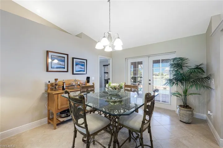 Dining space featuring french doors, light tile patterned floors, vaulted ceiling, and an inviting chandelier