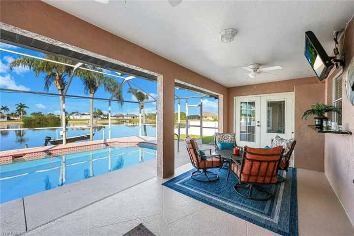 View of pool featuring glass enclosure, ceiling fan, a water view, a patio area, and a dock