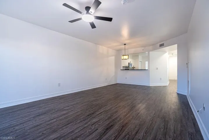 Unfurnished living room featuring dark wood-style flooring and a ceiling fan