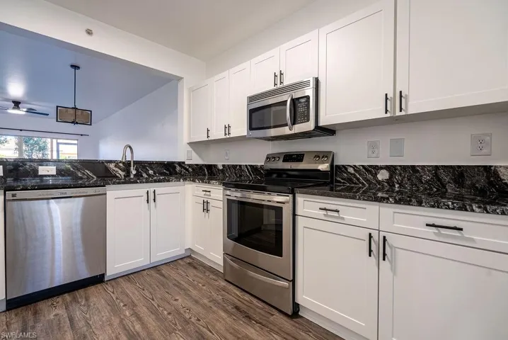 Kitchen featuring appliances with stainless steel finishes, white cabinetry, dark stone countertops, decorative light fixtures, and dark wood finished floors