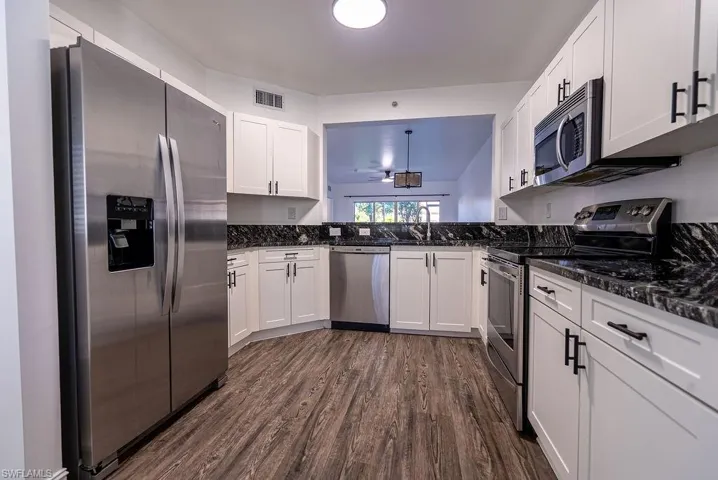 Kitchen featuring stainless steel appliances, white cabinetry, dark stone countertops, dark wood-style flooring, and decorative light fixtures