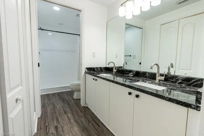 Full bathroom with double vanity, a shower stall, dark wood finished floors, and recessed lighting