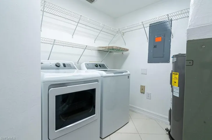 Washroom with electric panel, electric water heater, separate washer and dryer, and light tile patterned flooring