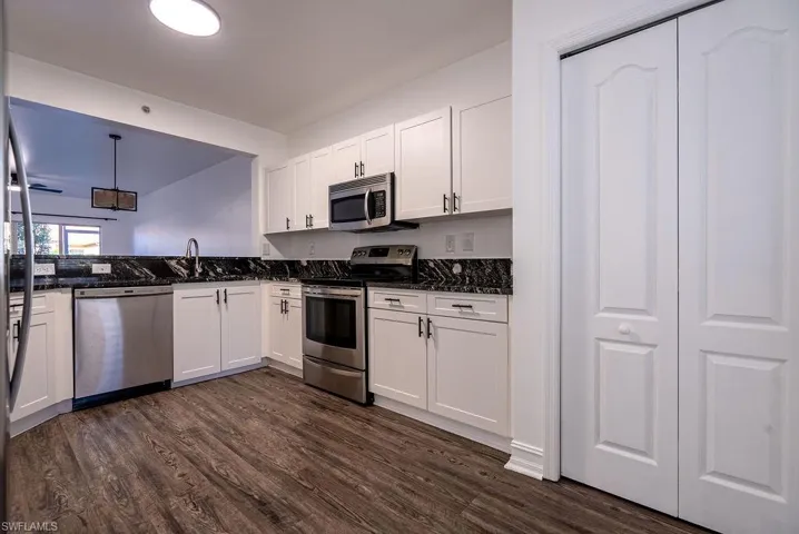 Kitchen featuring stainless steel appliances, white cabinetry, pendant lighting, and dark wood finished floors