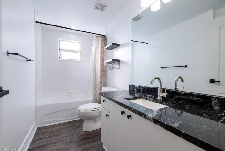 Bathroom featuring shower / tub combo with curtain, vanity, and dark wood-type flooring