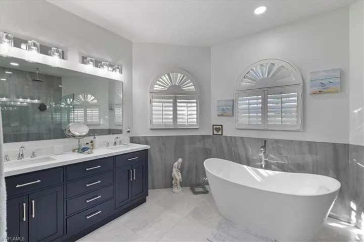Full bathroom with double vanity, a freestanding tub, a wainscoted wall, a stall shower, and tile walls