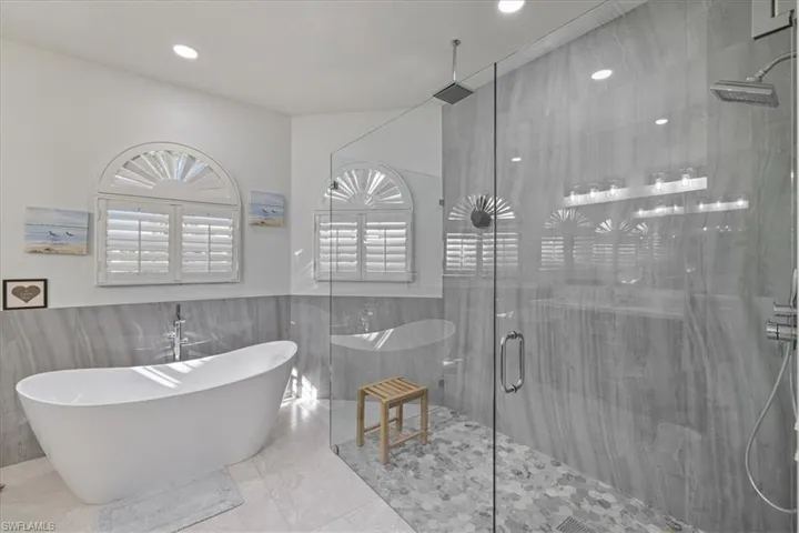 Bathroom with a freestanding bath, a shower stall, tile walls, wainscoting, and marble tiled flooring