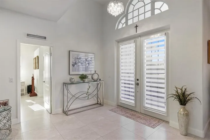 Foyer with french doors, a chandelier, light tile patterned floors, and a high ceiling