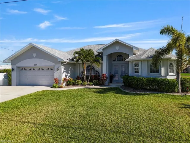 Ranch-style home with stucco siding, a front yard, driveway, a garage, and french doors