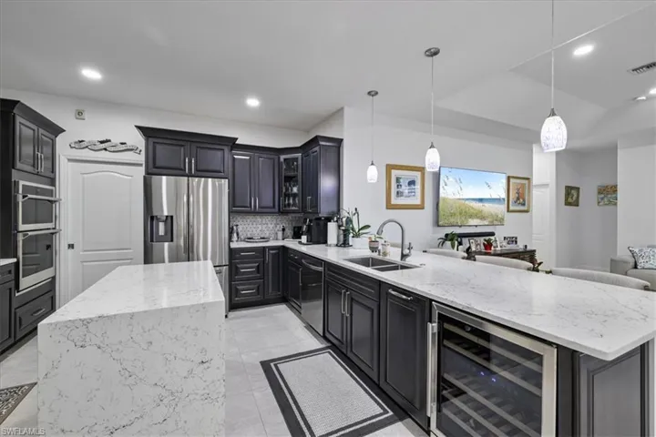 Kitchen featuring light stone counters, dark cabinetry, pendant lighting, beverage cooler, and recessed lighting