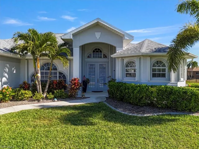Property entrance with a lawn, stucco siding, french doors, and roof with shingles