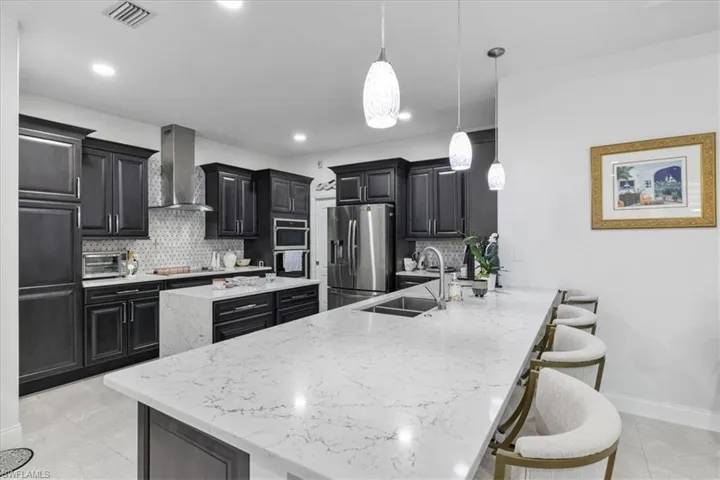Kitchen with dark cabinetry, light stone countertops, decorative light fixtures, decorative backsplash, and recessed lighting