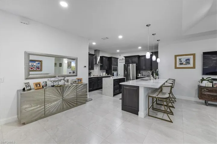 Kitchen with dark cabinets, a peninsula, light stone counters, a breakfast bar area, and backsplash