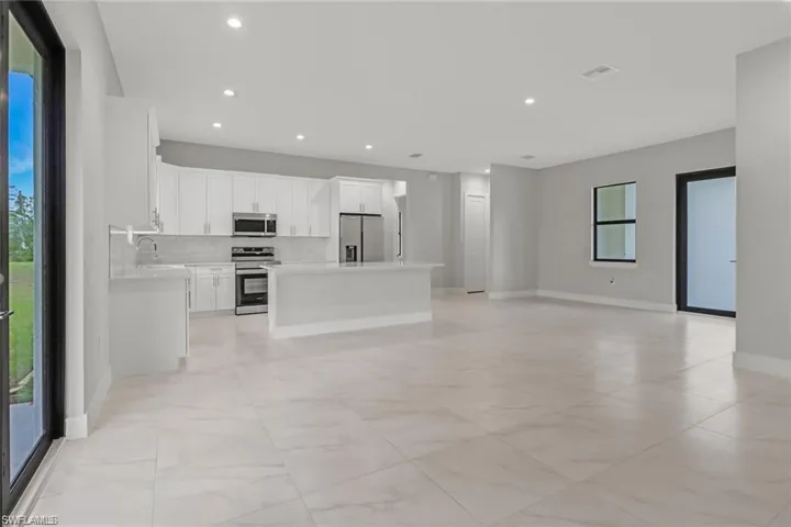 Kitchen featuring decorative backsplash, stainless steel appliances, sink, white cabinetry, and a kitchen island