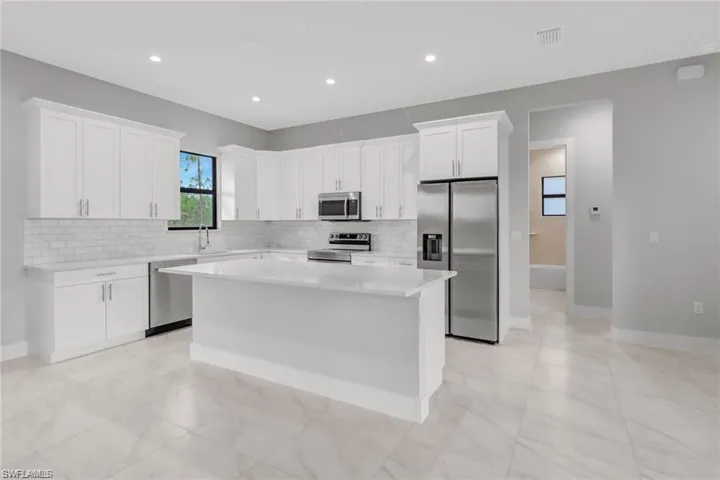 Kitchen featuring white cabinets, a kitchen island, appliances with stainless steel finishes, and tasteful backsplash