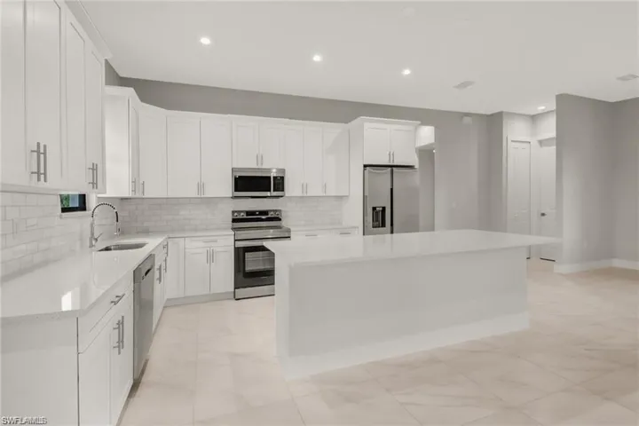 Kitchen featuring decorative backsplash, stainless steel appliances, sink, white cabinetry, and a kitchen island
