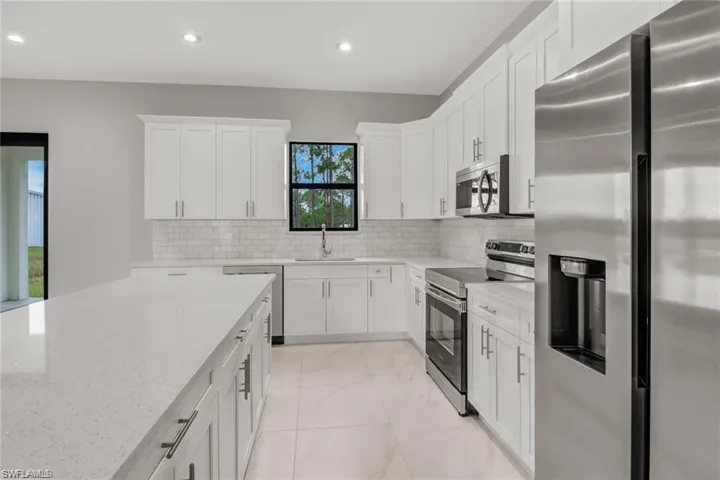 Kitchen with backsplash, white cabinets, sink, light stone counters, and stainless steel appliances