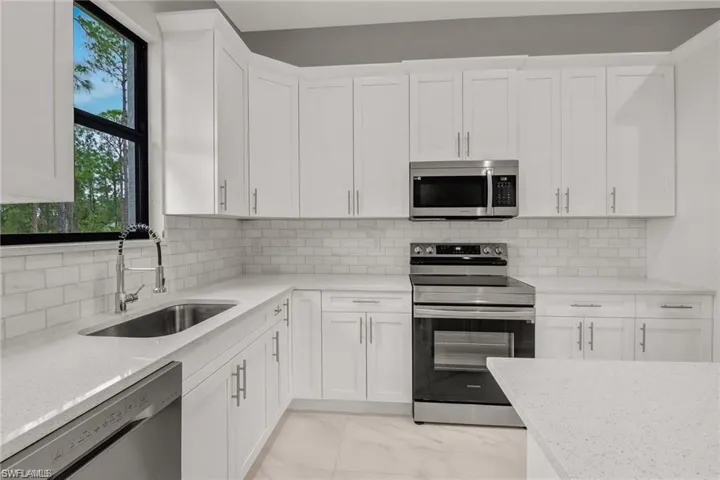 Kitchen with decorative backsplash, light stone counters, stainless steel appliances, sink, and white cabinets
