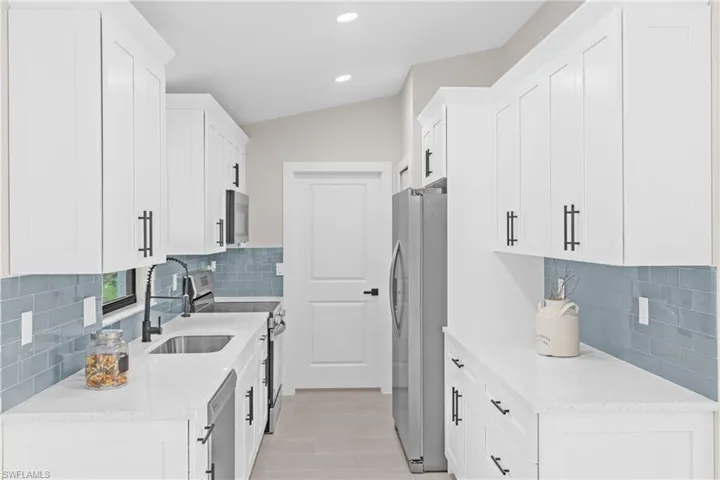 Kitchen with light stone counters, white cabinetry, stainless steel appliances, backsplash, and recessed lighting