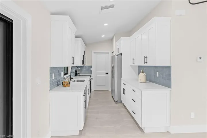 Kitchen with light stone countertops, white cabinets, stainless steel appliances, recessed lighting, and decorative backsplash