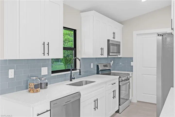 Kitchen with stainless steel appliances, white cabinets, light stone counters, decorative backsplash, and light wood-style flooring