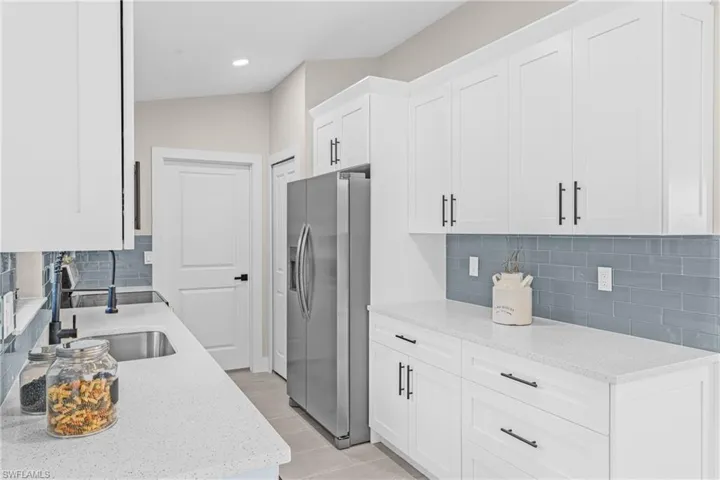 Kitchen featuring stainless steel fridge, light stone counters, white cabinets, backsplash, and recessed lighting