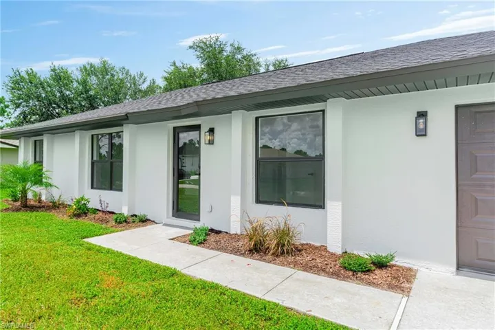 Property entrance with a yard, stucco siding, and a shingled roof