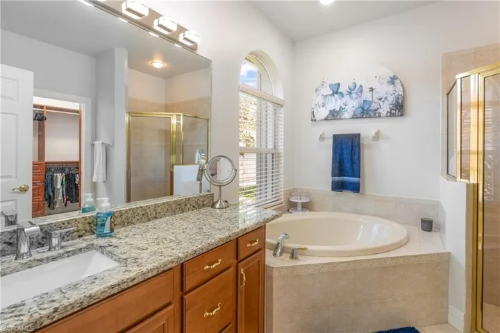 Full bathroom with vanity, a walk in closet, a garden tub, and a stall shower