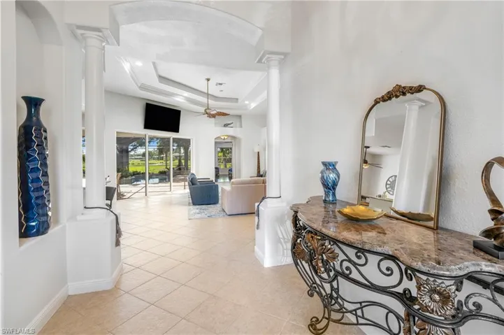 Hall featuring arched walkways, a tray ceiling, light tile patterned flooring, and decorative columns