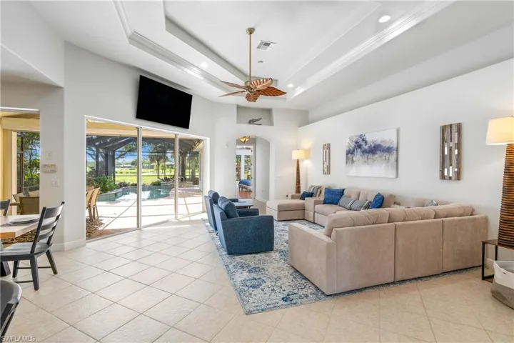 Living area featuring a tray ceiling, recessed lighting, light tile patterned floors, a high ceiling, and ceiling fan