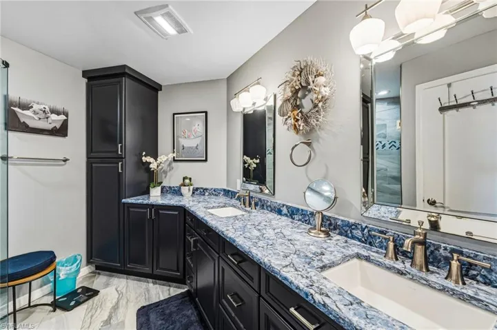 The reimagined primary bath exudes refined elegance, showcasing exquisite blue-veined granite, dual vanities with sleek square vessel sinks, abundant storage, and custom designer mirrors complemented by sophisticated lighting.