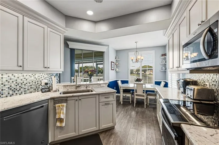 A beautifully redesigned kitchen overlooking the tranquil lake, showcasing exquisite blue-veined granite countertops and matching backsplash, enhanced by ambient under-cabinet lighting, recessed illumination, and a suite of premium stainless steel appliances.