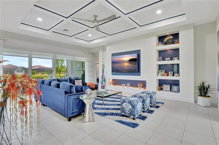 Living room featuring built in shelves, coffered ceiling, ceiling fan, and light tile flooring