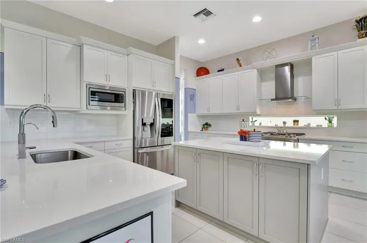 Kitchen featuring stainless steel appliances, backsplash, light tile floors, wall chimney exhaust hood, and sink, transom window