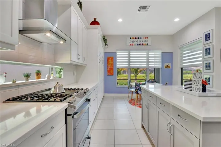 Kitchen with wall chimney range hood, backsplash, white cabinets, range with gas cooktop, and light tile floors, kitchen island