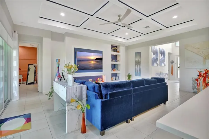 Living room with coffered ceiling, light tile flooring, ceiling fan, and entertainment unit