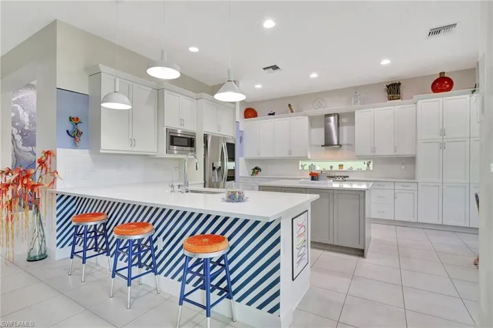 Kitchen with stainless steel appliances, wall chimney exhaust hood, sink, tasteful backsplash, and a kitchen bar, island