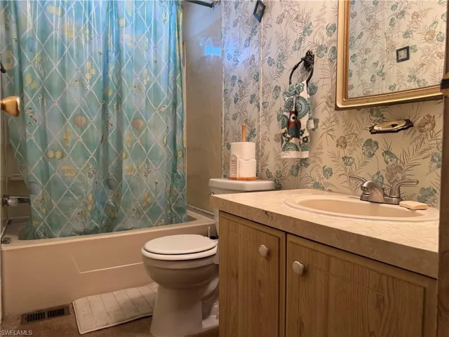 Bathroom with shower / bath combo with shower curtain, wallpapered walls, and vanity