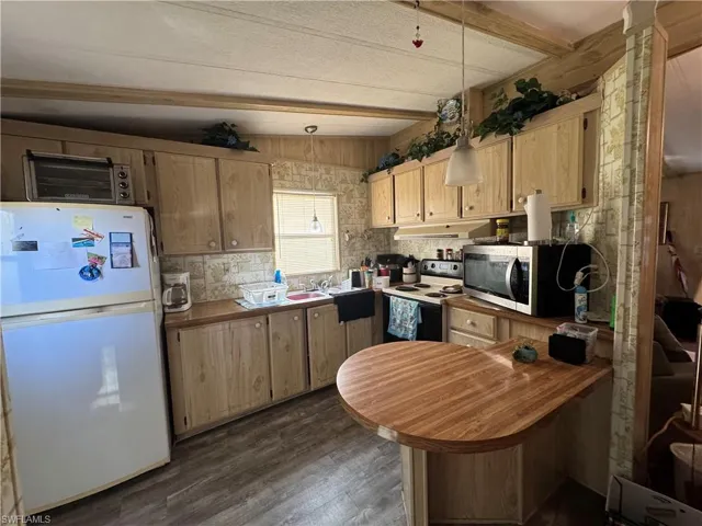 Kitchen with freestanding refrigerator, a peninsula, electric range oven, stainless steel microwave, and dark wood-style flooring