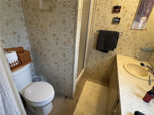 Full bathroom with wallpapered walls, vanity, and a shower stall