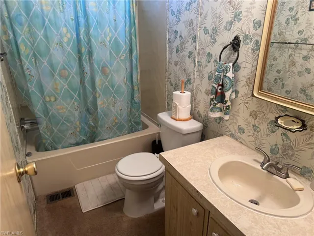 Full bathroom featuring wallpapered walls, shower / tub combo, and vanity