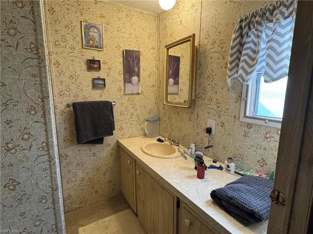 Full bathroom with wallpapered walls, vanity, and a shower with curtain