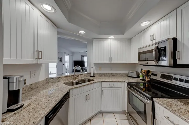 Kitchen with white beadboard cabinets, granite countertops, stainless steel appliances, tray ceiling. Breakfast bar and pass-through to family room and main dining area.