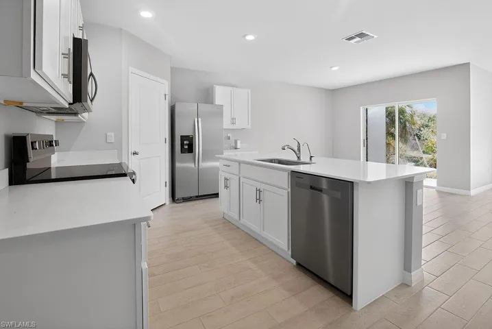 Kitchen with stainless steel appliances, white cabinets, recessed lighting, a kitchen island with sink, and light stone countertops