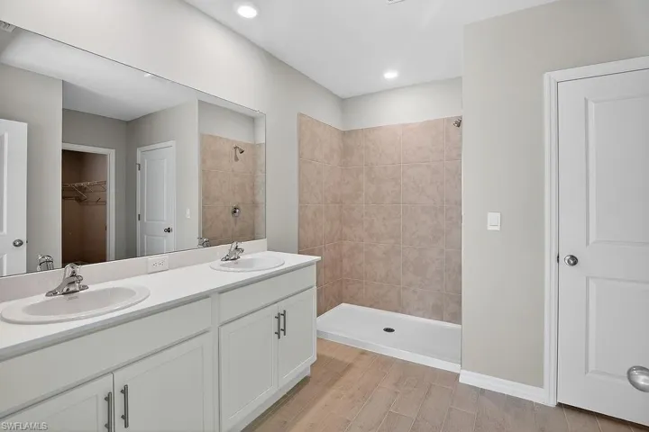 Full bathroom featuring a walk in closet, double vanity, tiled shower, and light wood-type flooring