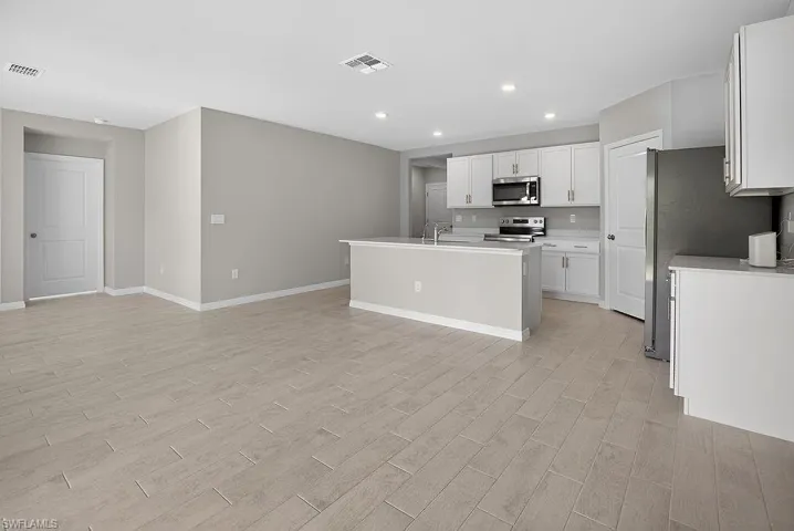 Kitchen featuring a kitchen island with sink, recessed lighting, stainless steel appliances, light wood-style flooring, and open floor plan