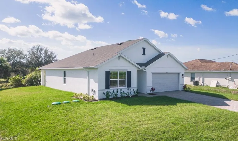 Ranch-style home featuring a front lawn, decorative driveway, stucco siding, an attached garage, and roof with shingles
