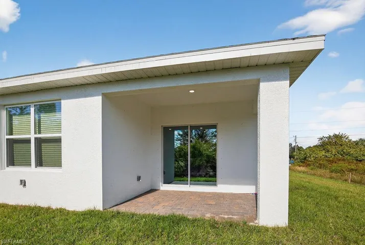 Entrance to property with stucco siding, a patio, and a lawn